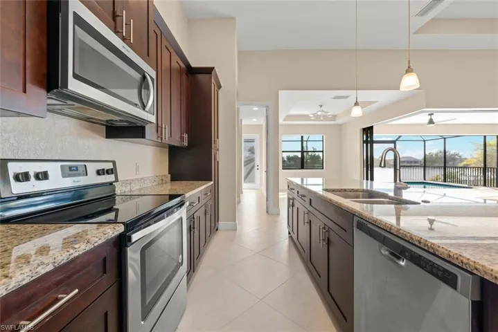 Kitchen with sink, a tray ceiling, pendant lighting, stainless steel appliances, and light stone countertops