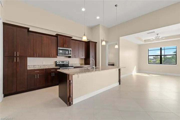 Kitchen featuring appliances with stainless steel finishes, decorative light fixtures, a breakfast bar area, a kitchen island with sink, and light stone countertops