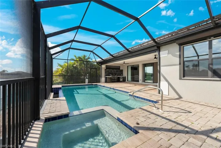 View of pool with ceiling fan, a patio, glass enclosure, an in ground hot tub, and an outdoor kitchen