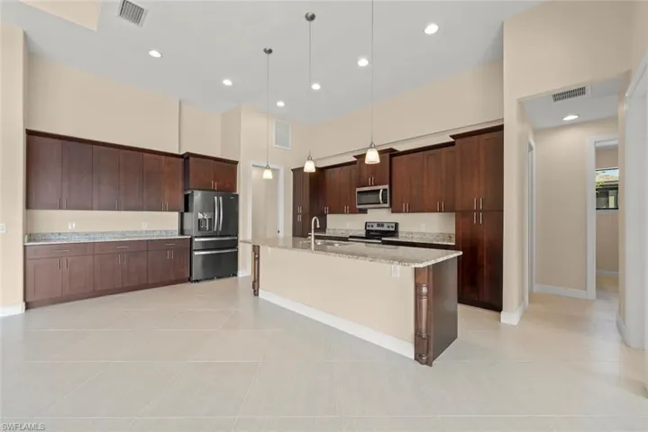 Kitchen with a breakfast bar area, stainless steel appliances, dark brown cabinetry, an island with sink, and decorative light fixtures