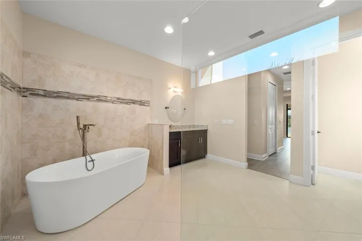 Bathroom featuring vanity, a tub to relax in, tile patterned flooring, and tile walls