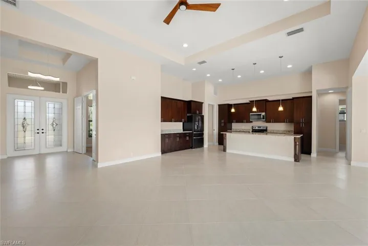 Unfurnished living room with light tile patterned floors, ceiling fan, a towering ceiling, a tray ceiling, and french doors