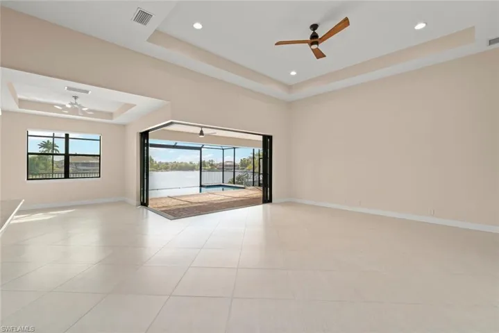 Unfurnished room with a water view, ceiling fan, a raised ceiling, and light tile patterned floors