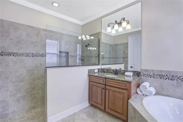 Full bathroom featuring vanity, walk in shower, a bath, ornamental molding, and tile patterned floors