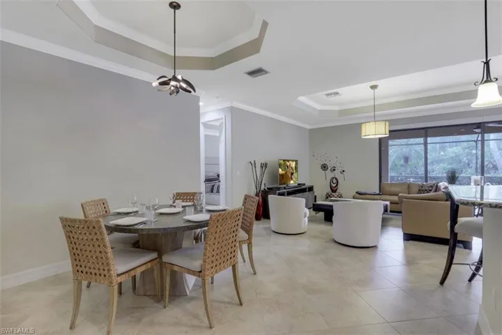 Dining area with a raised ceiling, crown molding, a chandelier, and light tile patterned floors