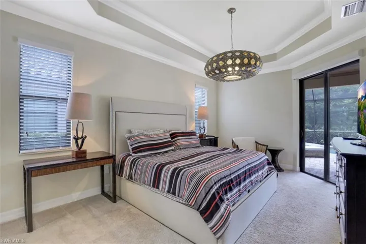 Bedroom featuring a tray ceiling, carpet floors, access to exterior, multiple windows, and crown molding