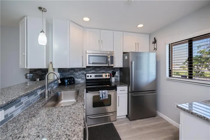 Kitchen featuring stainless steel appliances, tasteful backsplash, white cabinetry, light stone counters, and recessed lighting