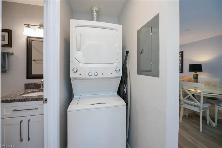 Laundry area featuring electric panel, stacked washing machine and dryer, and wood finished floors