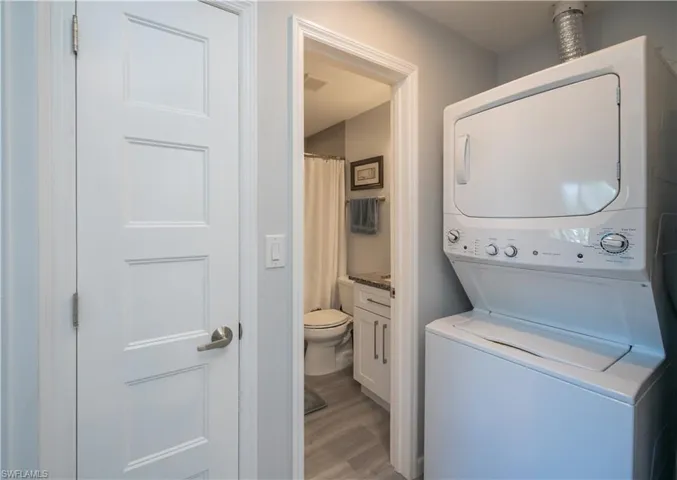 Washroom with light wood-type flooring and stacked washing machine and dryer
