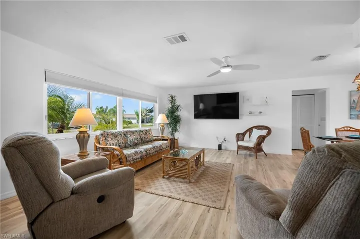 Spacious living area featuring expansive windows, wood-finish flooring, a ceiling fan, and white walls
