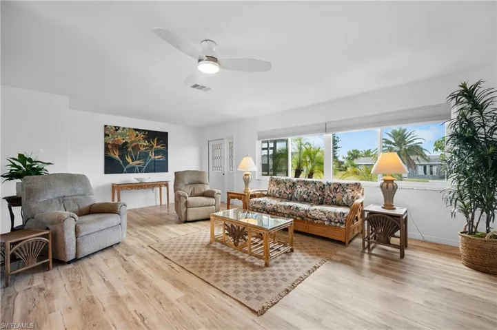 Spacious living area featuring light wood-finish flooring, a contemporary ceiling fan with integrated lighting, and multiple large windows