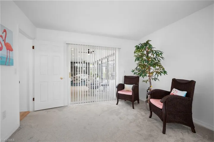 Carpeted room with a white paneled door, vertical blinds covering a glass slider, and light-colored walls