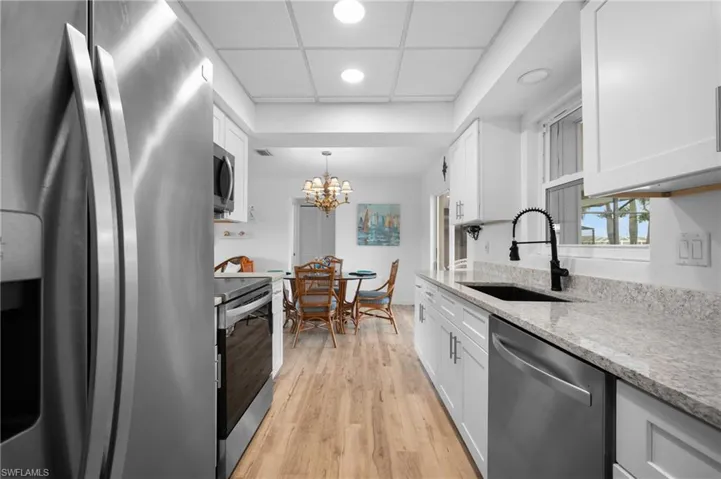 Galley kitchen featuring stainless steel appliances, white cabinetry, light-toned countertops, a black sink, and a contrasting black faucet