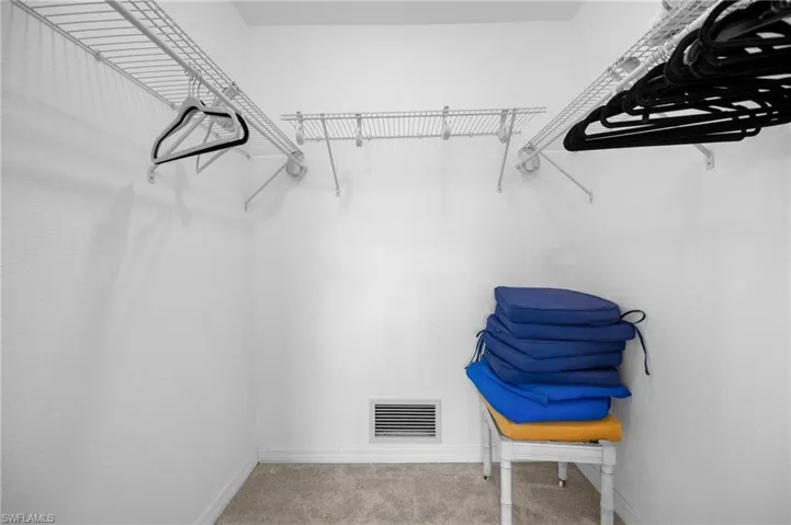 Walk-in closet featuring wire shelving, wire hanging rods, light gray carpet flooring, white painted walls, and a floor-level vent