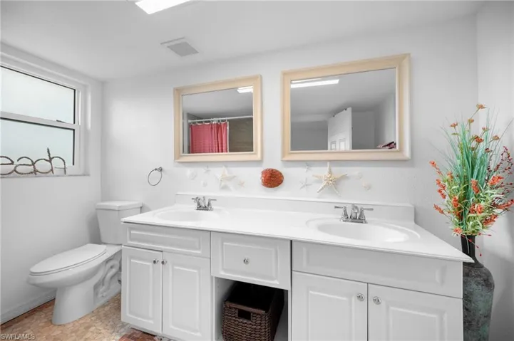 Bathroom featuring a double vanity with white cabinetry, integrated sinks, and individual framed mirrors