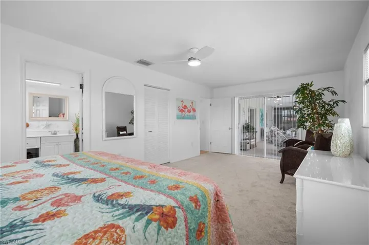 Carpeted bedroom featuring white walls, a ceiling fan with integrated lighting, bi-fold closet doors, and sliding glass doors with vertical blinds leading to an enclosed space