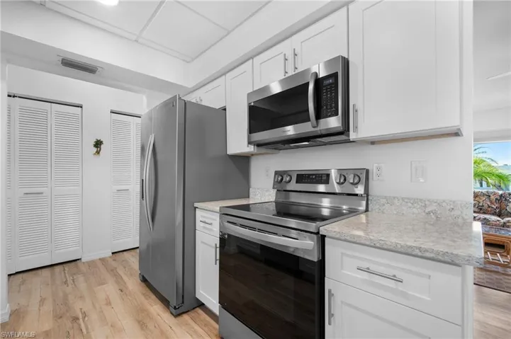 Kitchen featuring stainless steel appliances, white cabinetry, light countertops, wood-finish flooring, and louvered bifold closet doors