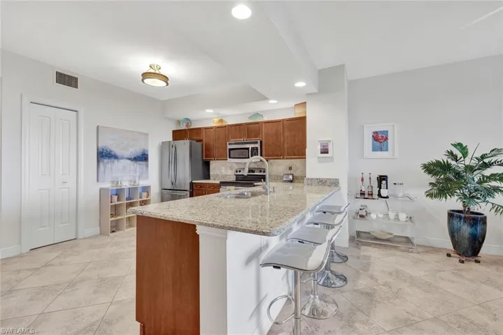Kitchen featuring a large island with stone countertop, stainless steel appliances, wood cabinetry, and tile flooring