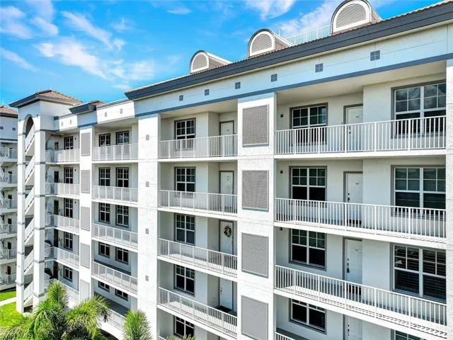 Multi-story building featuring individual balconies with white railings, multiple window units, and exterior wall sconces