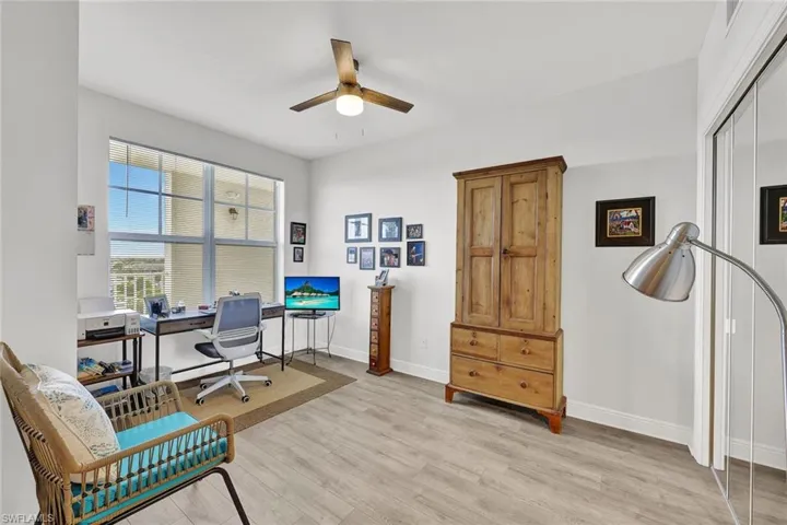 High ceilings with a ceiling fan, large window with balcony railing, light wood-finish flooring, and white walls