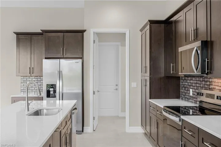 Kitchen with decorative backsplash, appliances with stainless steel finishes, dark brown cabinets, light stone countertops, and light tile patterned floors