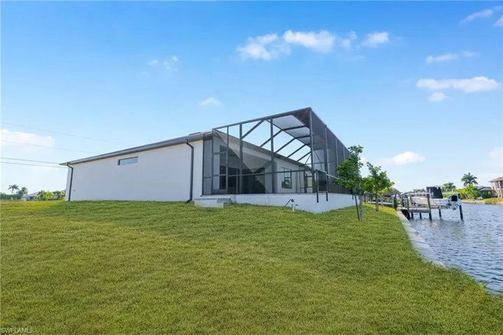 Back of house featuring a sunroom, a lawn, glass enclosure, stucco siding, and a water view