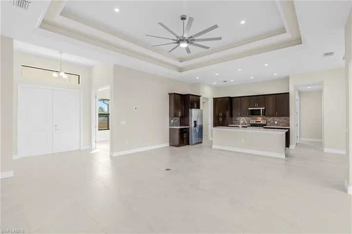 Unfurnished living room with a raised ceiling, recessed lighting, a ceiling fan, and light tile patterned flooring