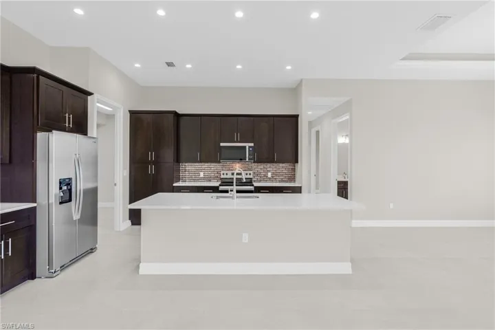 Kitchen featuring stainless steel appliances, dark brown cabinets, decorative backsplash, a kitchen island with sink, and recessed lighting
