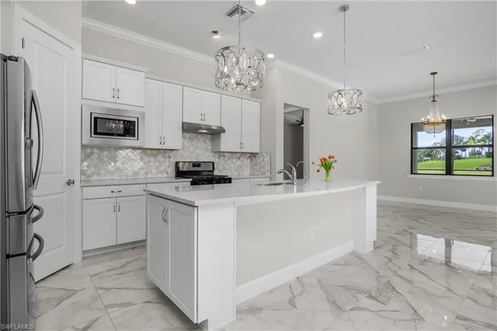 Kitchen with a kitchen island with sink, decorative light fixtures, white cabinets, and appliances with stainless steel finishes