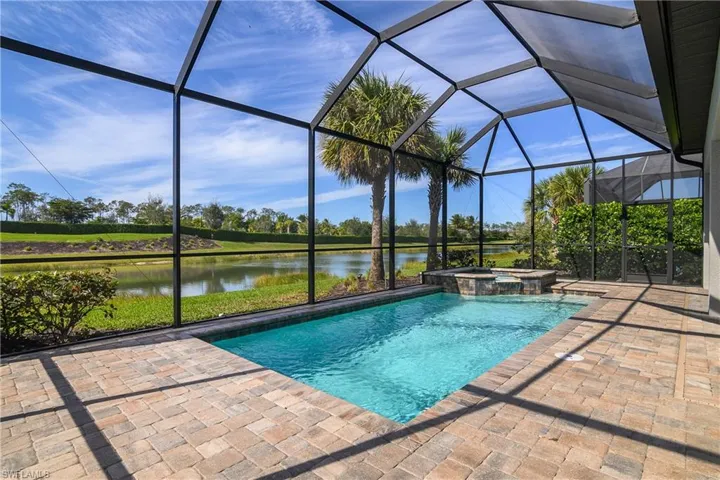 View of pool featuring an in ground hot tub, a water view, a patio area, and glass enclosure