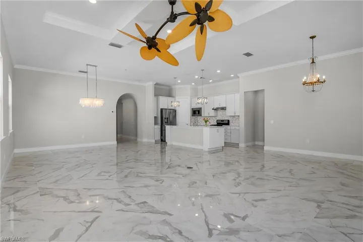 Great room with open living, dining, and kitchen features decorative fans, crown molding, tray ceilings, and spacious kitchen with lots of storage space.