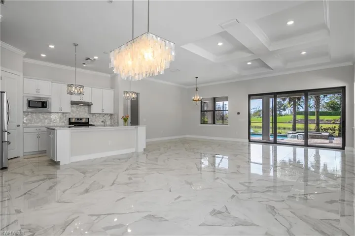 Beautiful Open Floor Plan features white cabinets, coffered ceiling, crown molding, kitchen, dining, great room, and beautiful lighting fixtures.