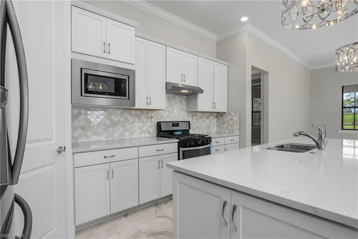 Kitchen with sink, stainless steel appliances, light stone counters, white cabinets, and decorative backsplash
