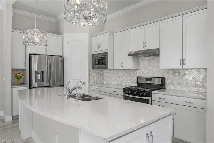 Kitchen featuring sink, white cabinetry, pendant lighting, stainless steel appliances, and an oversized kitchen island with sink and reverse osmosis system.