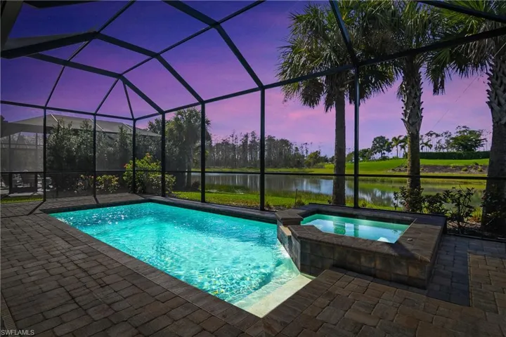 Pool at dusk featuring an in ground hot tub, a patio, screened enclosure, and a water view