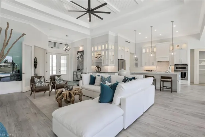 Living room with ceiling fan with notable chandelier, crown molding, light wood-type flooring, and a high ceiling