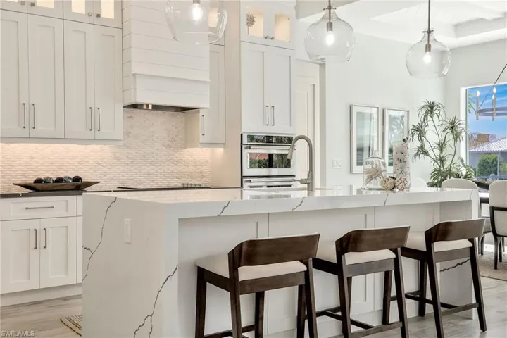 Kitchen featuring light hardwood / wood-style floors, custom exhaust hood, pendant lighting, and tasteful backsplash