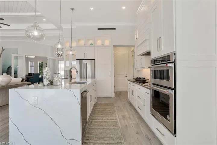 Kitchen with white cabinetry, light hardwood / wood-style flooring, light stone countertops, appliances with stainless steel finishes, and a spacious island
