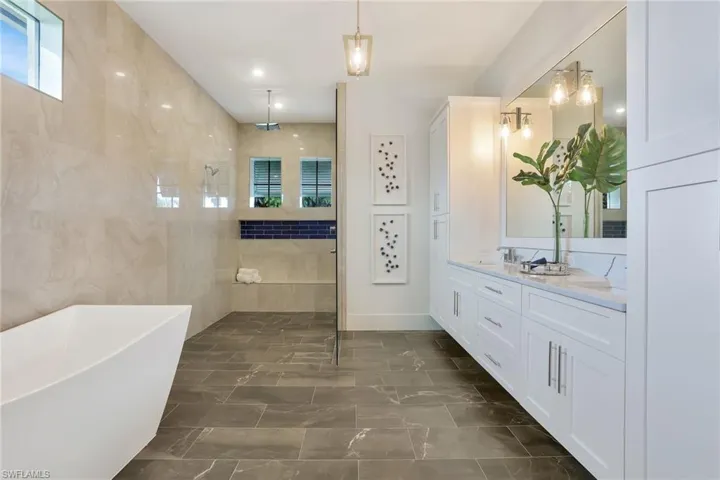Bathroom featuring tile patterned flooring, tile walls, a tub, and dual bowl vanity