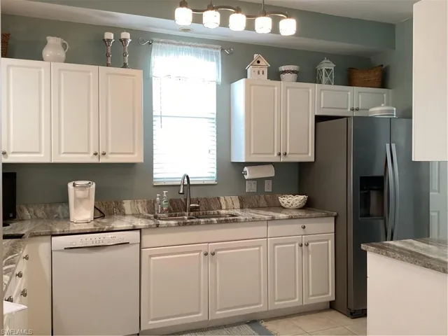 Kitchen featuring dishwasher, hanging light fixtures, sink, fridge, and white cabinetry