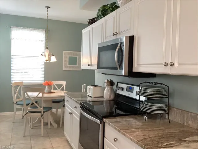 Kitchen with white cabinets, plenty of natural light, decorative light fixtures, and stainless steel stove