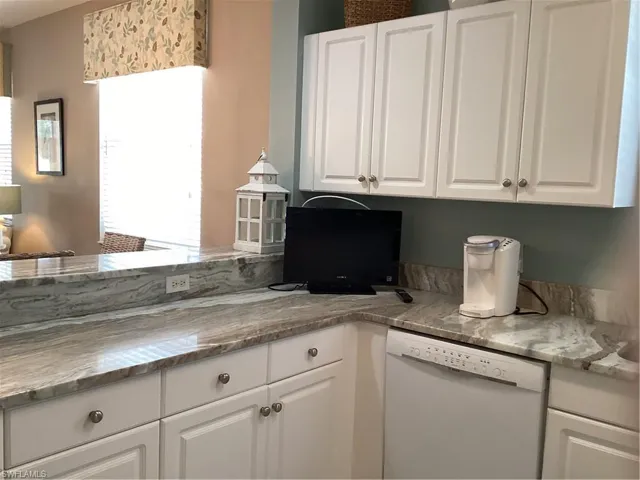Kitchen with dishwasher, white cabinetry, and light stone counters