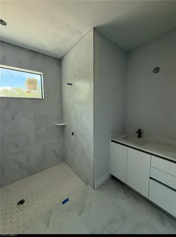 Bathroom featuring vanity, a marble finish shower, and marble look tile flooring