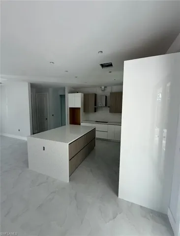 Kitchen with modern cabinets, white cabinetry, light marble finish flooring, black cooktop, and wall chimney exhaust hood