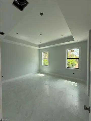 Unfurnished room featuring a tray ceiling and light marble finish flooring