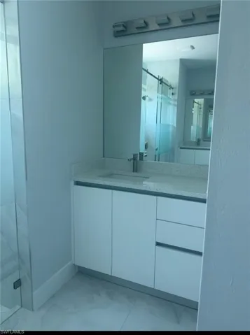 Full bath with light marble finish floors, a marble finish shower, and vanity