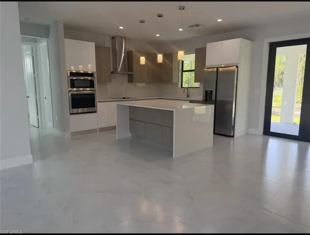 Kitchen with modern cabinets, stainless steel appliances, hanging light fixtures, wall chimney exhaust hood, and white cabinetry