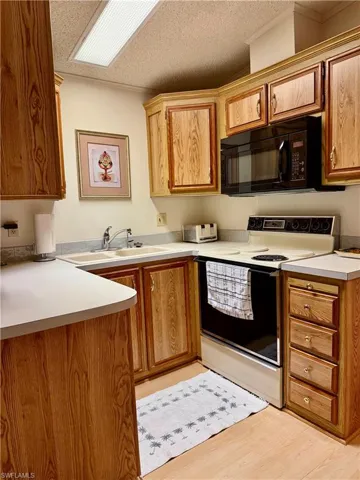 Kitchen featuring white electric range, light countertops, black microwave, light wood-style flooring, and a textured ceiling