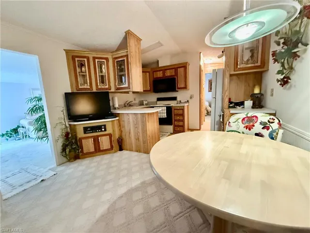 Kitchen with light countertops, a peninsula, white appliances, glass insert cabinets, and vaulted ceiling