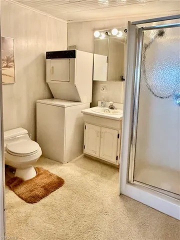 Full bath with vanity, a stall shower, stacked washer and dryer, light carpet, and light flooring